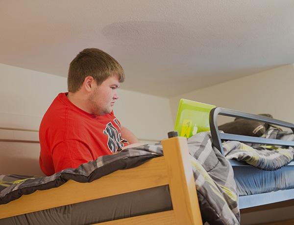 一个男生拿着笔记本电脑躺在高架床上.
