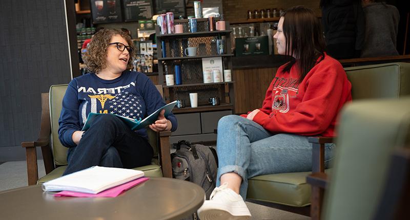 两个女人坐在舒适的椅子上，在咖啡店里聊天.